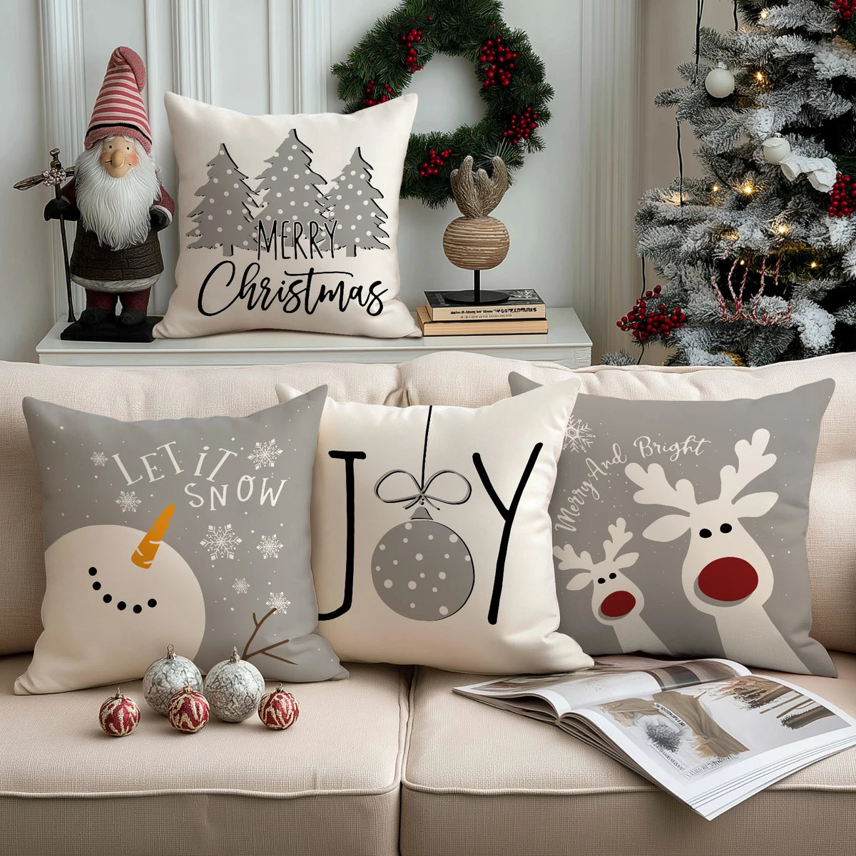 Housses de coussin de Noël Snowman, Joy et Rudolph sur un canapé crème avec une couronne et un sapin enneigé