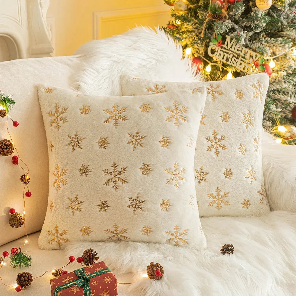 Housse de coussin déco Noël Snow Beige à flocons métallisés sur un fauteuil devant un sapin illuminé