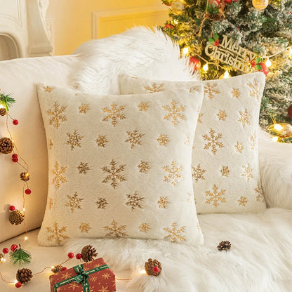 Housse de coussin déco Noël Snow Beige à flocons métallisés sur un fauteuil devant un sapin illuminé