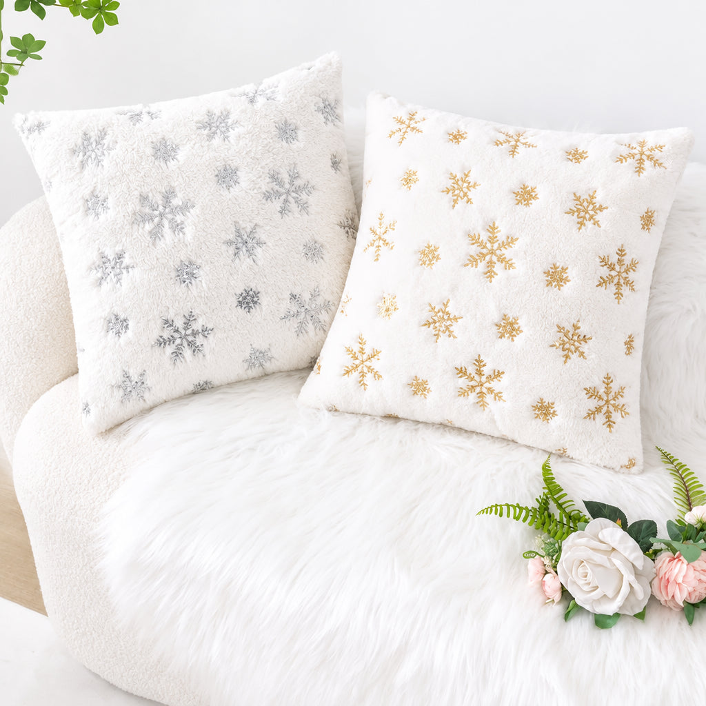Deux housses de coussin déco Noël Snow à flocons Argent et Or sur un canapé clair