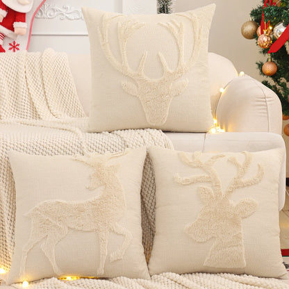 Trois housses de coussin de Noël Renne Ivoire en bouclette sur un canapé devant un sapin