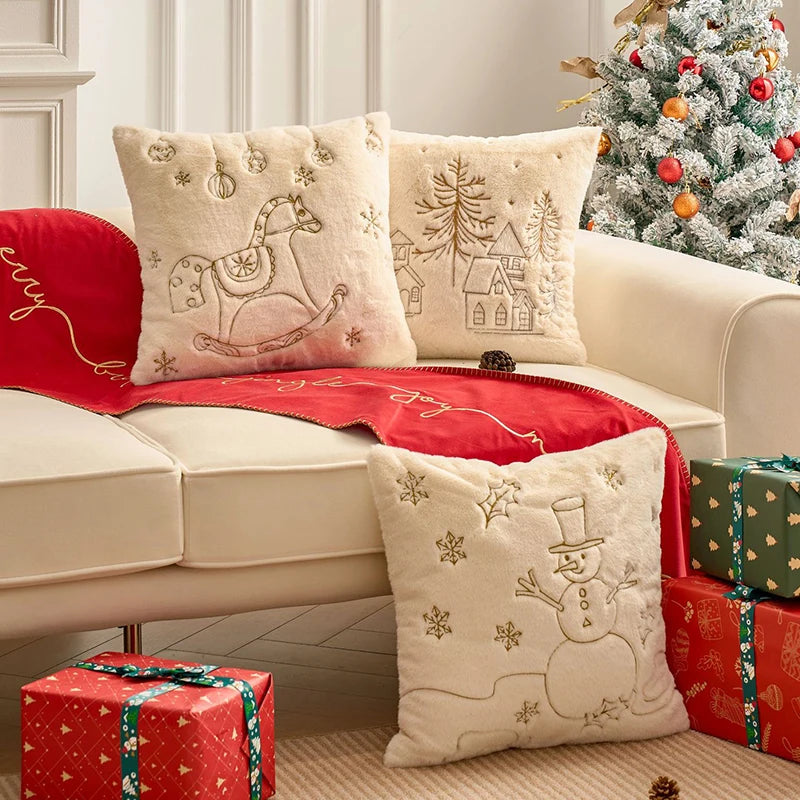 Housses de coussin de Noël Écru avec cheval à bascule, sapin et bonhomme de neige en fil Doré sur un canapé