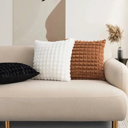 Housses de coussin Velours Gaufré Noir, Blanc et Camel alignées sur un canapé clair