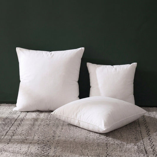 Coussins de garnissage blancs de tailles différentes posés sur un tapis gris devant un mur vert foncé